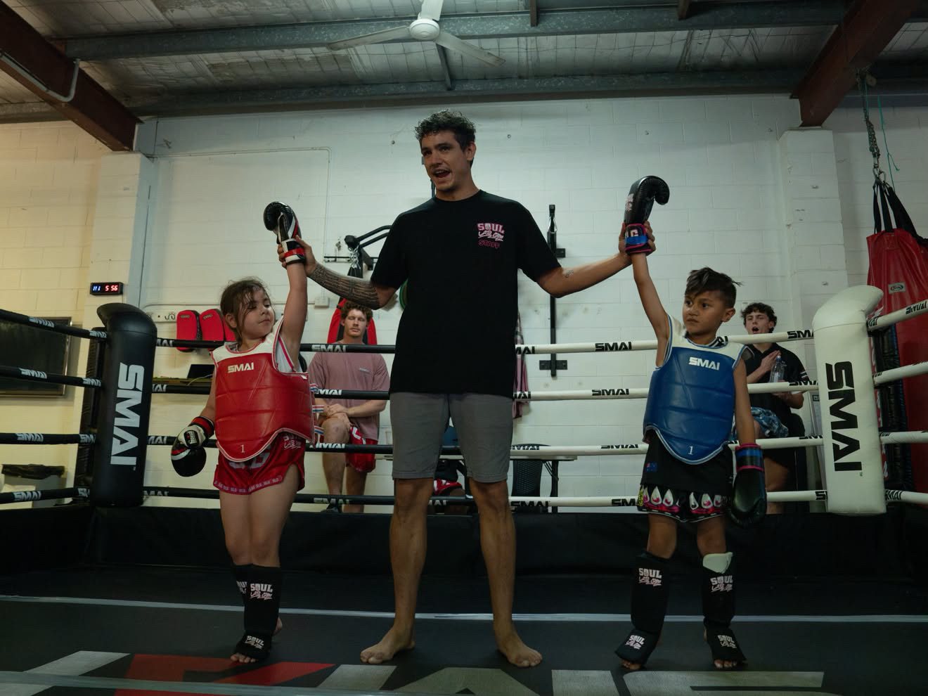 Two young fighters in chest guards with both hands raised after their junior bout
